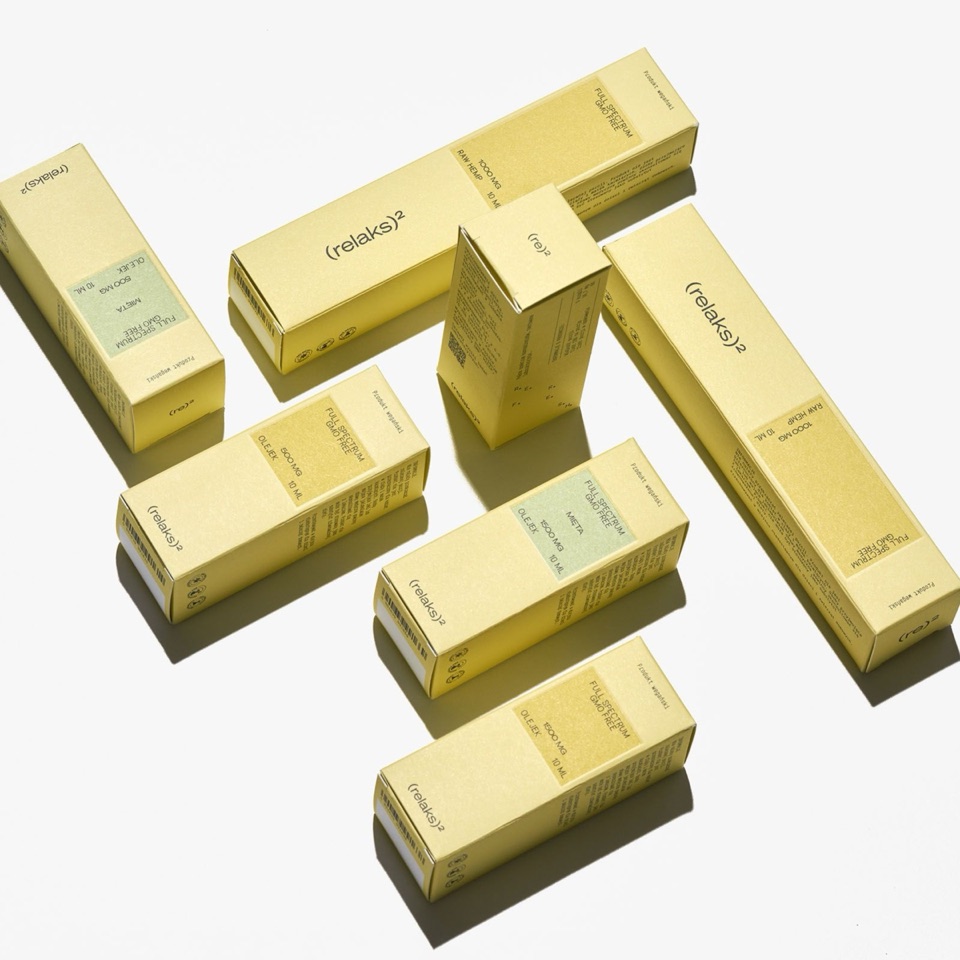 Range of tall gold folding cartons arranged around small cosmetic bottle formats